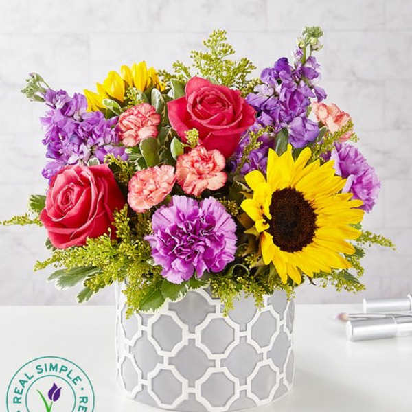 Mixed bouquet with roses, sunflowers, and purple blooms in a white vase