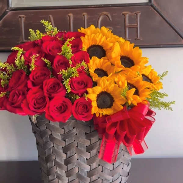 Red roses and yellow sunflowers arranged in a woven basket with a red ribbon
