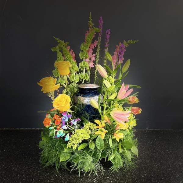 Tall floral arrangement with yellow roses, pink lilies, and purple spikes in a blue vase