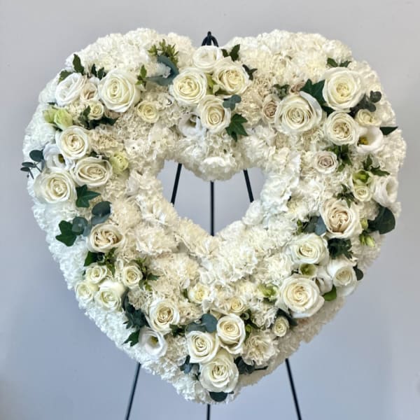 Heart-shaped white floral wreath with roses on a stand