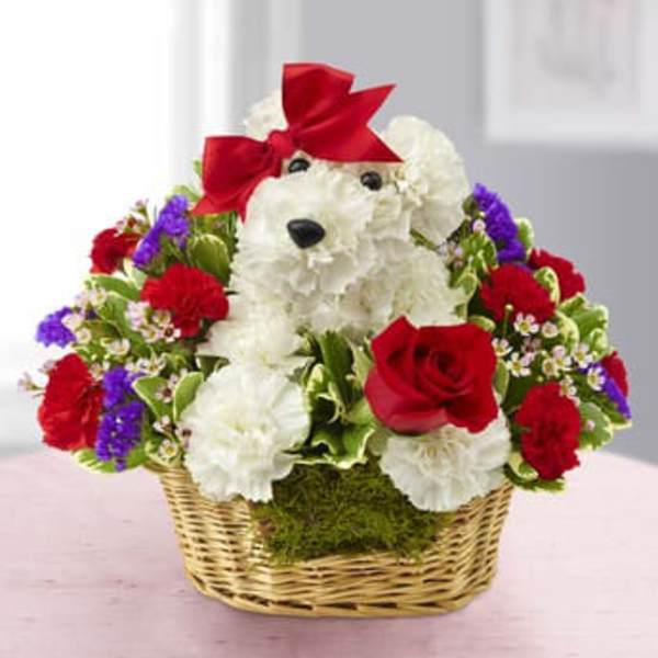 White teddy bear in a basket surrounded by red, white, and purple flowers