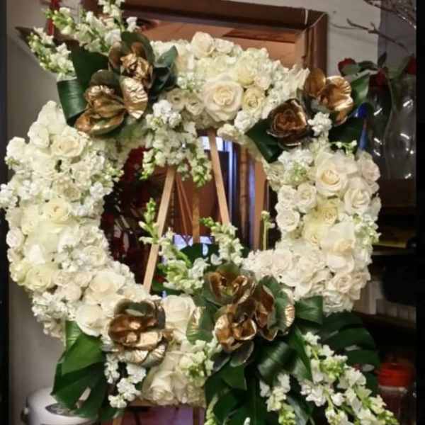 Large white floral wreath on a wooden easel with gold accents
