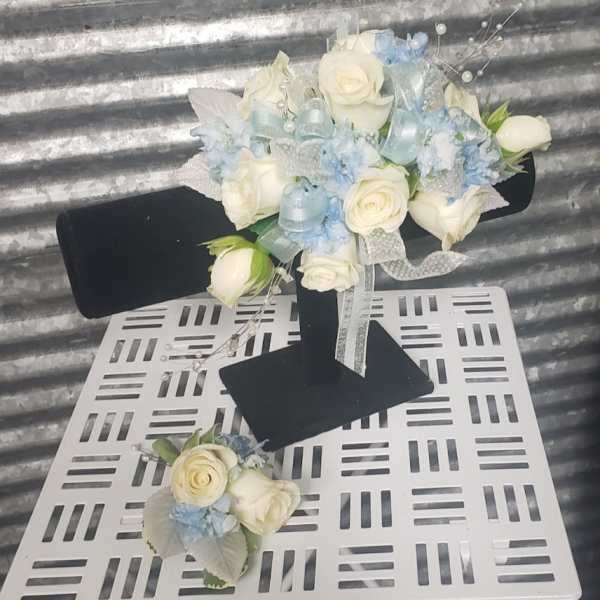 White rose bouquet with pale blue accents and ribbon on a black stand