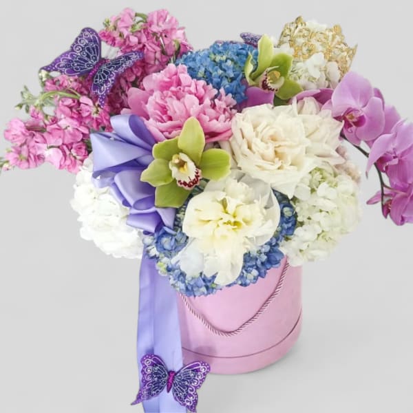 Pink hat box of mixed pink, white, blue, and green flowers with cascading orchids, ribbon, and butterflies.