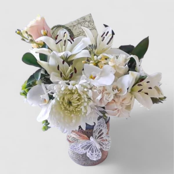 White and blush bouquet of lilies, orchids, and chrysanthemums in a wrapped glass vase with lace butterfly decoration.