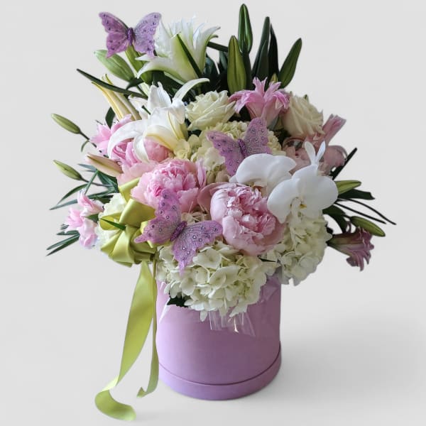 Pink and white bouquet with lilies, peonies, hydrangeas, and orchids in a pink hat box with ribbon and butterflies
