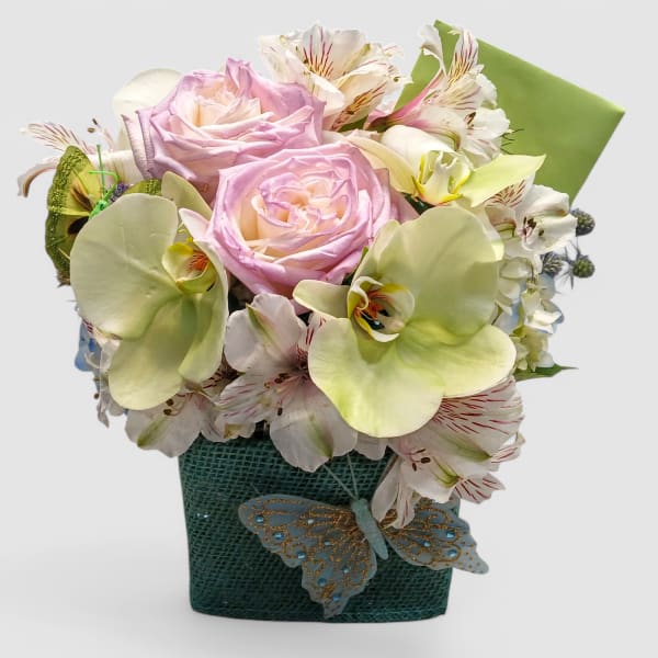 Pastel bouquet of lavender roses, white orchids, and alstroemeria in a green textured vase with butterfly accent
