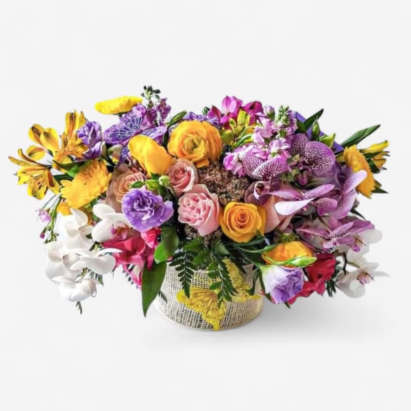 Low arrangement of bright yellow, pink, purple, and white flowers in a burlap-wrapped container