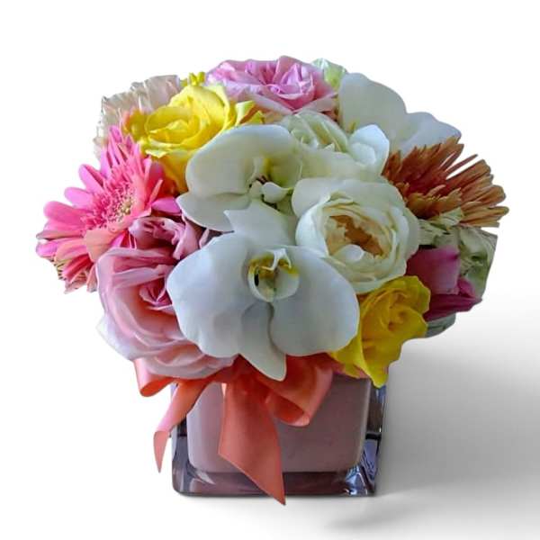 Colorful bouquet of roses, orchids, and gerbera daisies in a square glass vase