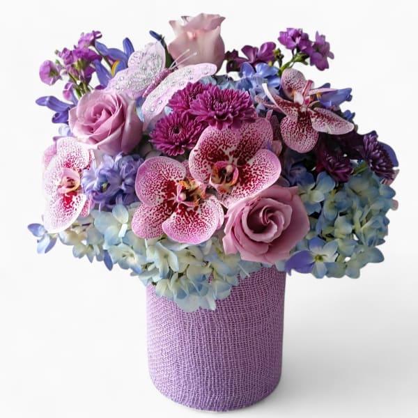Lavender, pink, and blue flower arrangement with orchids and roses in a textured lavender cylinder vase