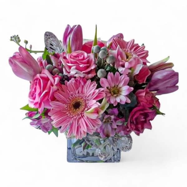Compact pink arrangement with roses, gerbera daisies, tulips, and mixed blooms in a square glass vase