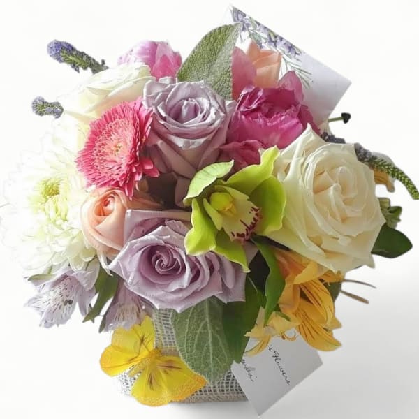 Round mixed bouquet of pastel roses, gerbera daisy, orchid, and other blooms in a small cube container with card.