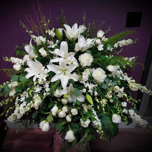 Large all-white floral arrangement with lilies, roses, and other blooms in a fan shape.