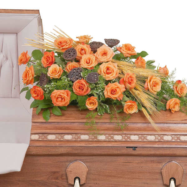 Orange rose casket spray with wheat accents arranged on a wooden casket