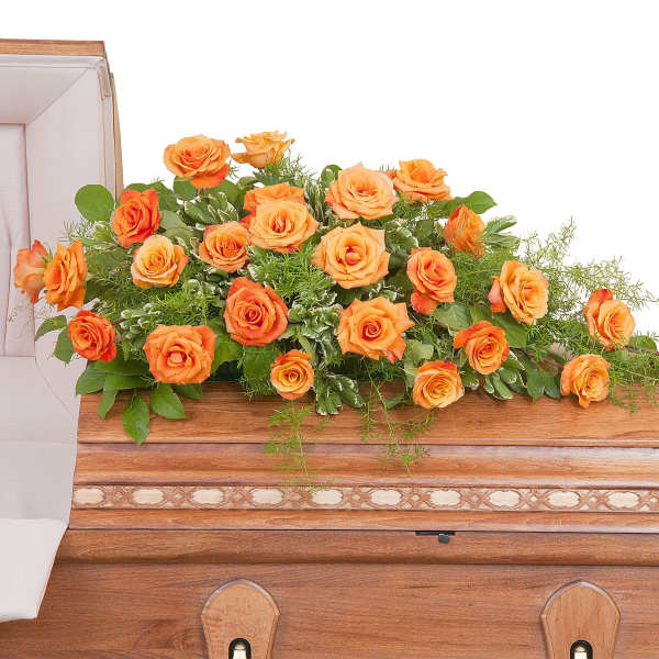 Long spray of orange roses arranged on top of a wooden casket