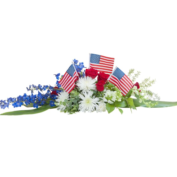 Low red, white, and blue floral centerpiece with American flags, roses, mums, and blue delphinium.