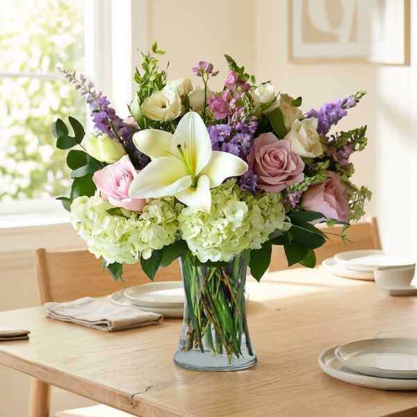 Bouquet of white lilies, roses, and purple flowers in a glass vase