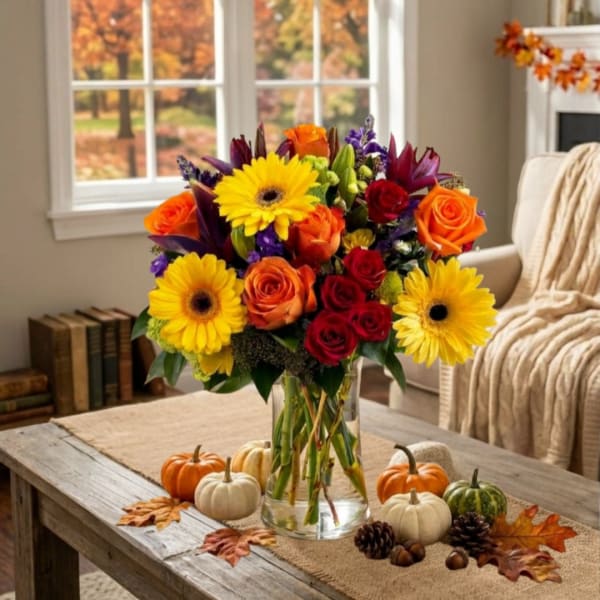 Mixed bouquet of roses and yellow daisies in a glass vase with small pumpkins