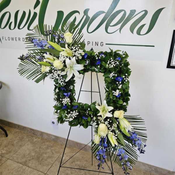Floral wreath on a black stand with white lilies and blue flowers