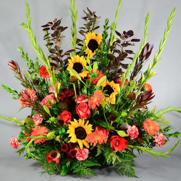 Large mixed bouquet with sunflowers, roses, gerbera daisies, and tall green spikes