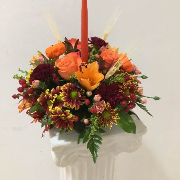 Orange and burgundy floral arrangement with a tall red candle