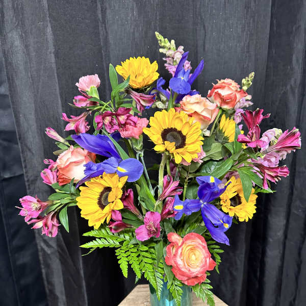 Mixed bouquet of sunflowers, roses, and purple iris in a blue vase