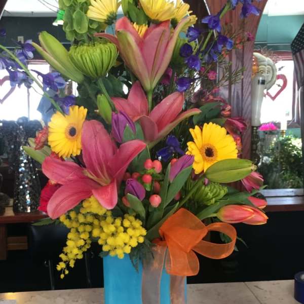 Tall mixed flower arrangement in a blue vase with orange ribbon