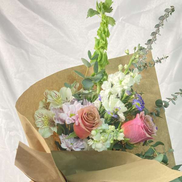 Hand-tied bouquet of pink roses, white blooms, and eucalyptus wrapped in brown paper