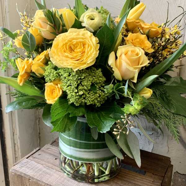 Yellow roses and green blooms arranged in a glass vase