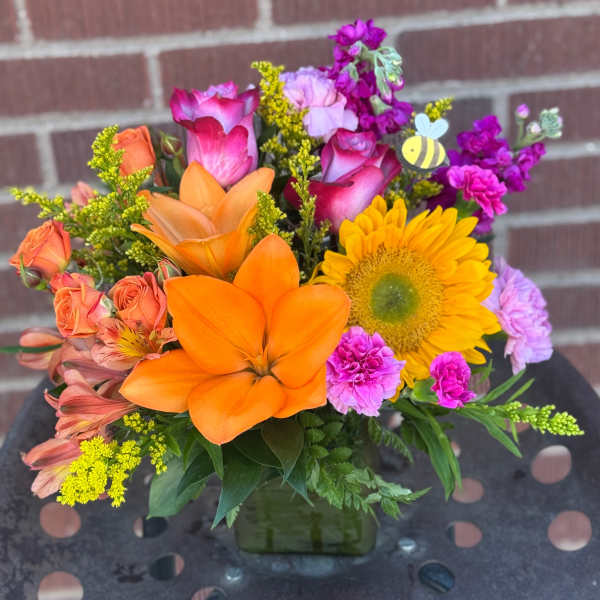 Colorful bouquet with orange lilies, yellow sunflower, and pink roses in a square vase