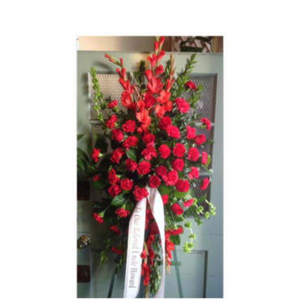 Tall standing spray of red carnations with a white ribbon