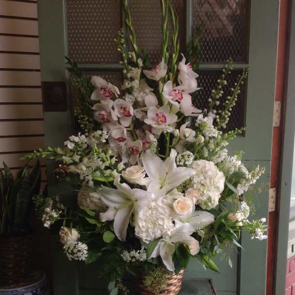 Tall white floral arrangement in a wicker basket with lilies and orchids