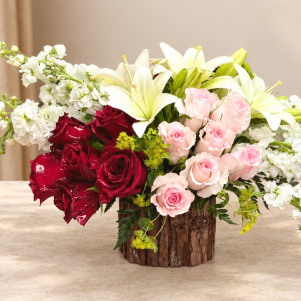 Bouquet of red and pink roses with white lilies in a rustic wood vase