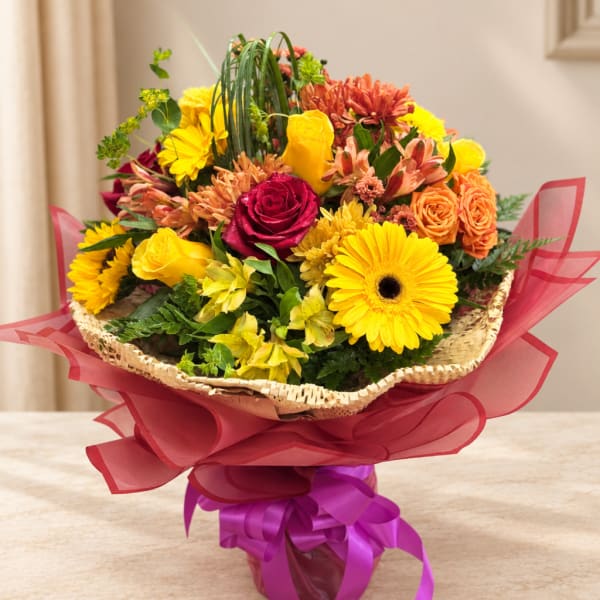 Mixed bouquet of yellow, orange, and pink flowers in a wrapped basket