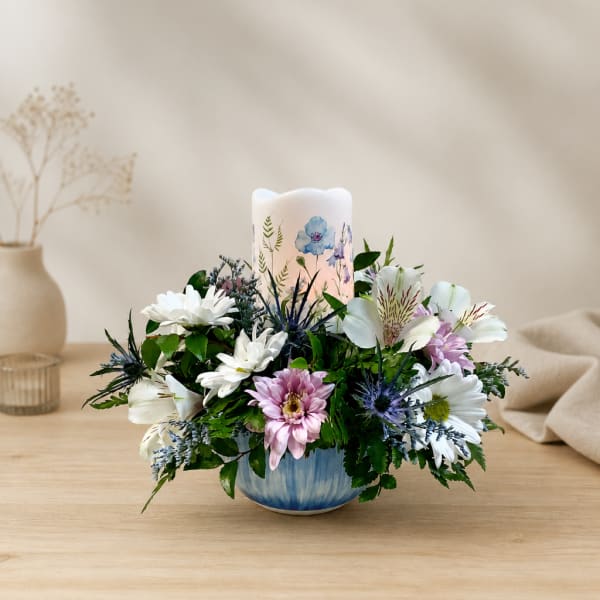 Mixed white and pink flowers arranged around a candle in a blue bowl