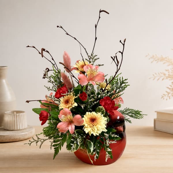 Mixed floral arrangement in a red vase with pink and yellow blooms