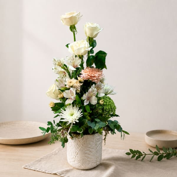 Tall floral arrangement with white roses and mixed blooms in a white textured vase
