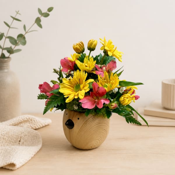 Yellow and pink flowers arranged in a small wooden bear-shaped vase
