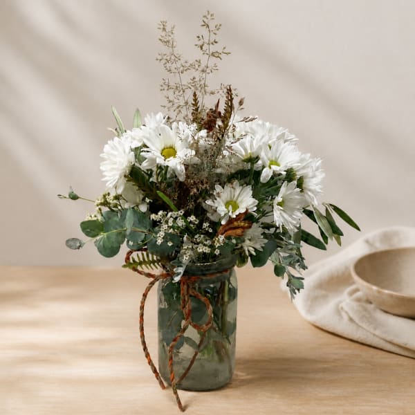 White daisy bouquet in a glass jar with a braided ribbon tie