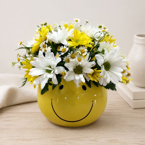 Yellow smiley-face vase filled with white and yellow daisies
