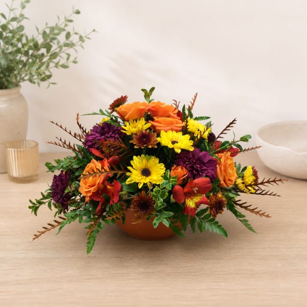 Mixed orange, yellow, and purple flowers in a low bowl arrangement