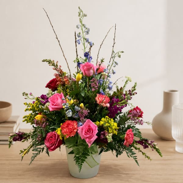 Mixed bouquet of roses, carnations, and snapdragons in a pale vase