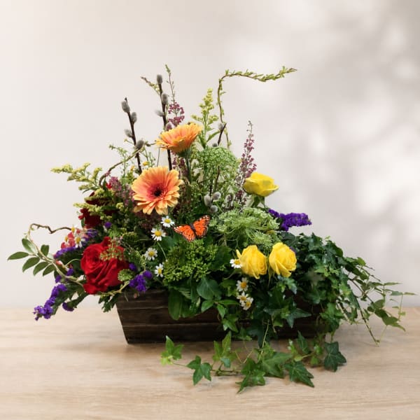 Mixed flower arrangement in a rectangular wooden planter with roses and daisies