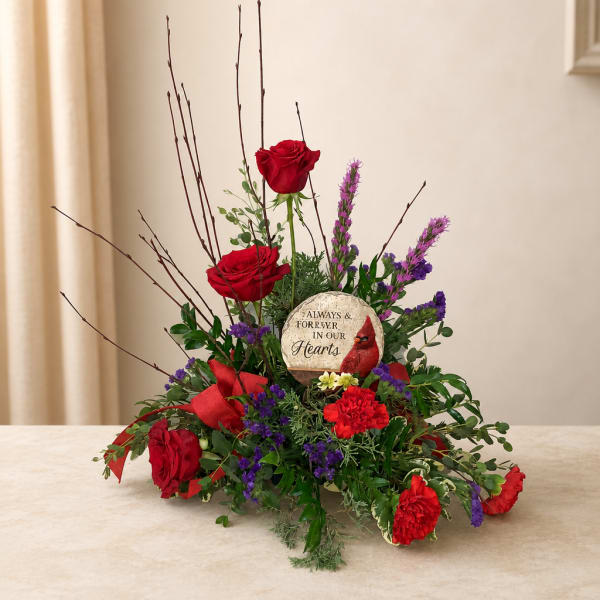 Red roses and purple flowers arranged around a memorial stone on a table