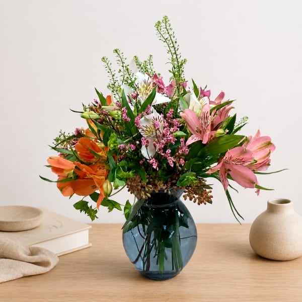 Mixed bouquet of pink, orange, and white flowers in a blue glass vase