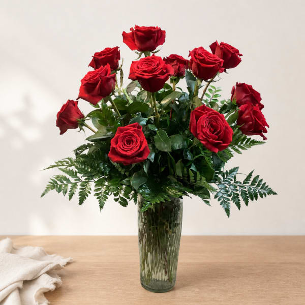 Red roses arranged in a clear glass vase with greenery