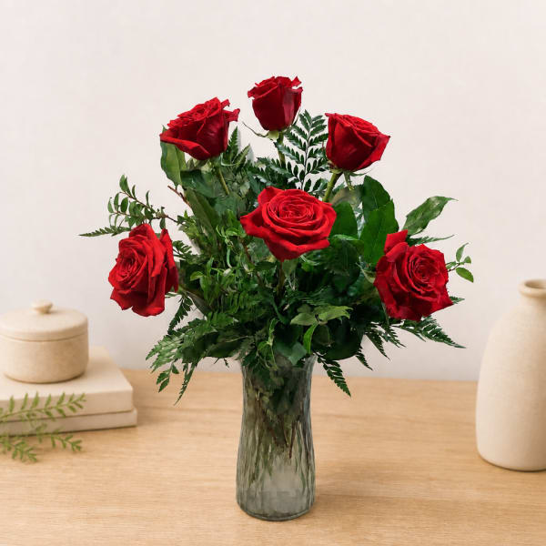 Red roses arranged in a clear glass vase with greenery