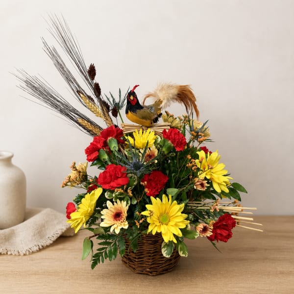 Basket arrangement with red and yellow flowers and a decorative bird topper