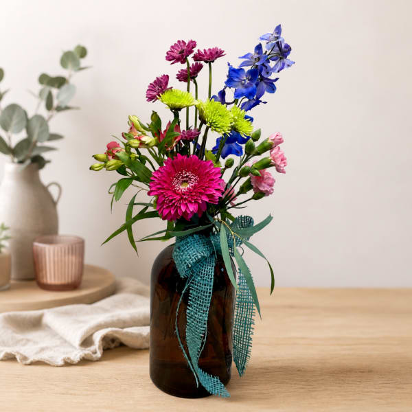 Colorful mixed bouquet in a dark glass vase with a teal ribbon