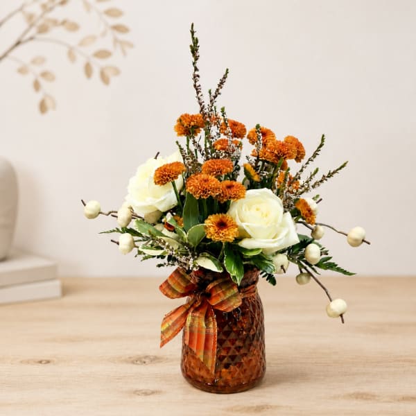 Orange and white flower arrangement in an amber vase with a plaid ribbon